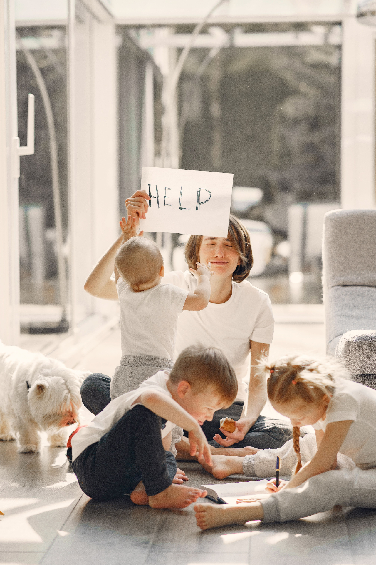 A parent holding a 'Help' sign surrounded by children — the everyday overwhelm we walk through with families